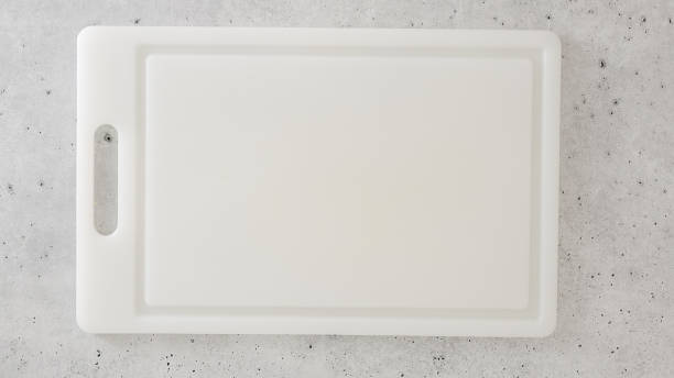 White plastic cutting board close-up on a gray stone kitchen countertop, flat lay, copy space