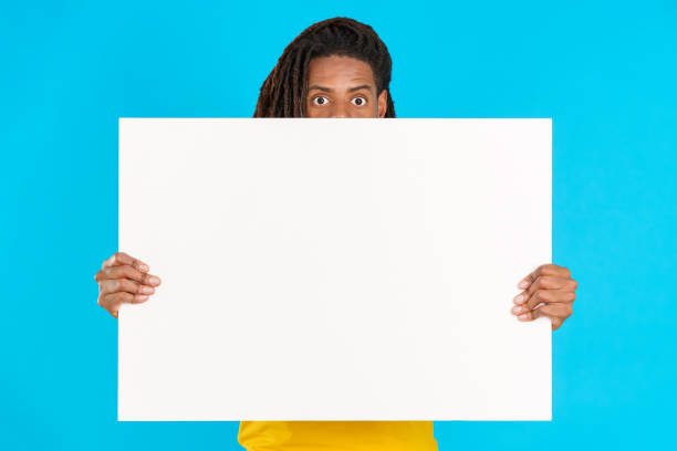 istock Surprised latin man with dreadlocks hiding behind a blank board 1491856850