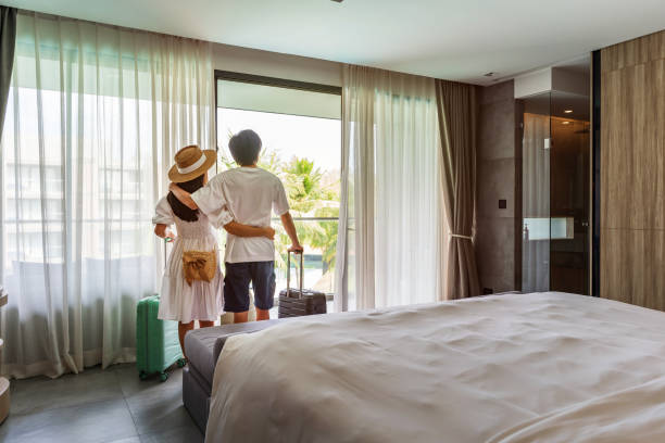 Young couple traveler opening the curtains and looking at the view from the window of a hotel room while on summer vacation, Travel lifestyle concept stock photo