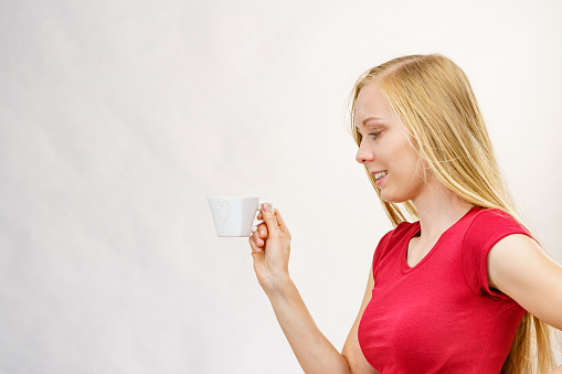 Blonde long hair woman with heart shaped coffee cup. Time to wake up, switching on. Copy space.