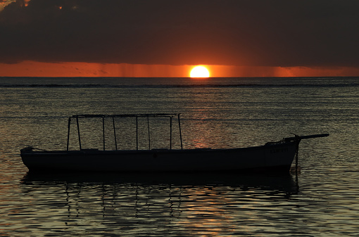 Albion, Mauritius - May 05, 2023: Vibrant colors during sunset at the Indian Ocean close the public beach with a fisherman boat in Albion in the West of Mauritius.