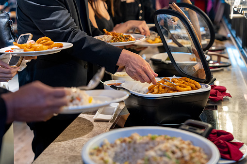 Business people are using service tongs to carefully select their food from the buffet line.