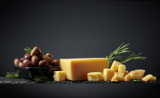 Parmesan cheese with olives and rosemary on a black background.