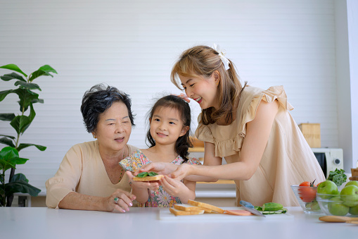Grandmother, mother and granddaughter prepare food in the kitchen. Multi generation and relationship concept.