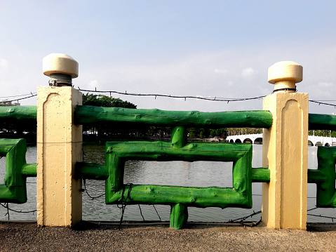 A concrete fence imitating wood by the lake. It prevents people from falling into the water. Fence around the lake. Green fence. Chinese style fence.