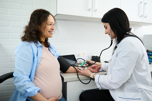 Female Obstetrician gynecologist doctor measuring blood pressure of the pregnant woman in the hospital. Pregnancy-induced Hypertension and prophylaxis of eclampsia and preeclampsia concept. Gynecology