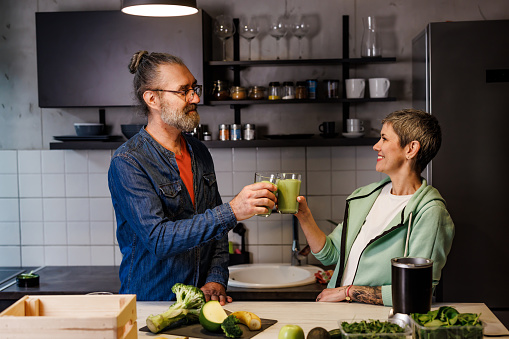 Happy mature couple drinking healthy green smoothie in kitchen