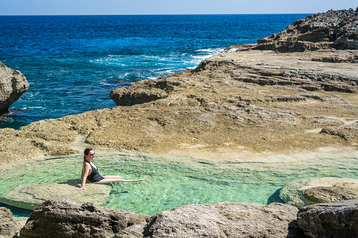 A young woman wearing a straw hat bathes in the beautiful and colorful waters of the Mediterranean Sea on a summer day on the beach of Monti Russu in Santa Teresa Gallura, facing the Strait of Bonifacio.