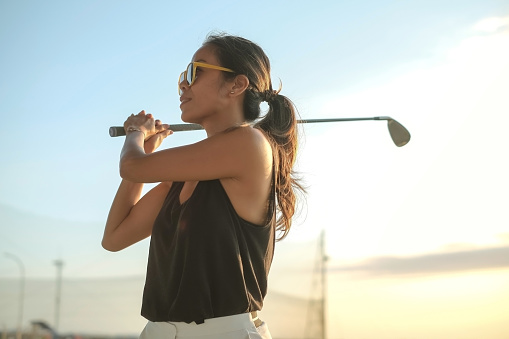 Close-up shot of a confident mature Asian woman swinging golf club at driving range
