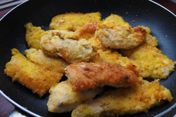 Fried chicken fillet in a black pan close-up. Many pieces of fried chicken, rolled in breadcrumbs. Homemade quick recipes for cooking and body processing of meat products
