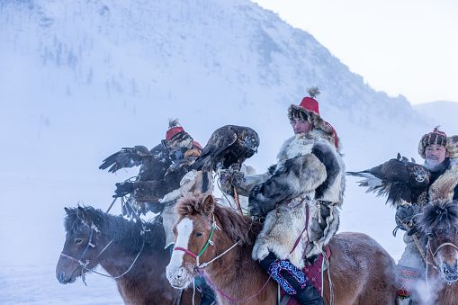Gorkhi-terelj National park,Ulaanbaatar,Mongolia 14 January 2023 : Traditional Kazakh eagle hunters in Mongolia riding on horseback through barren snowy mountains with their birds on their arms