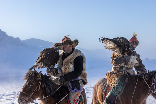 Gorkhi-terelj National park,Ulaanbaatar,Mongolia 14 January 2023 : Traditional Kazakh eagle hunters in Mongolia riding on horseback through barren snowy mountains with their birds on their arms