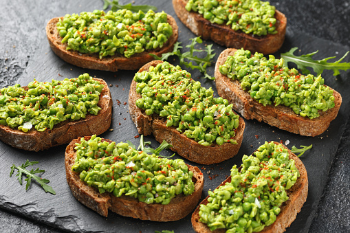 Mashed peas sourdough bread toast with sea salt flakes and chilli served on black slate.