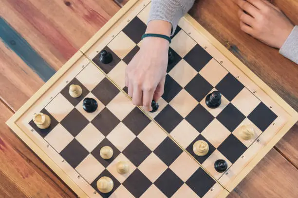 Table top view of the chess board with the hand of a teenage girl playing