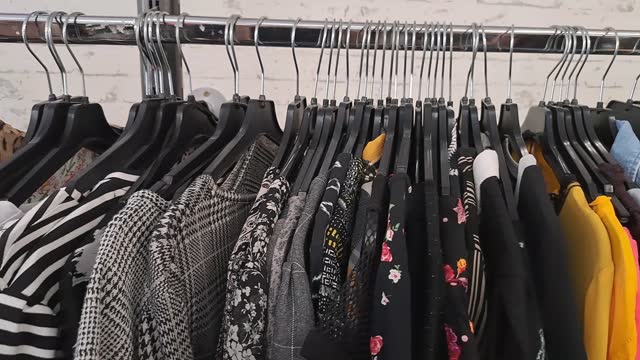 camera moves from left to right across clothing rack in thrift store, colorful tops hanging everywhere