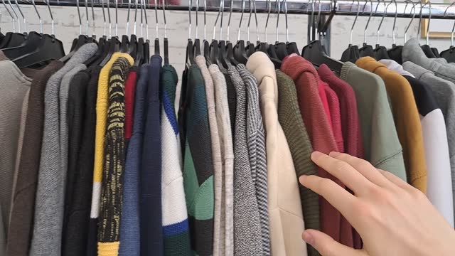 Touching fabric and searching through clothes rack in thrift store, man and unisex collection