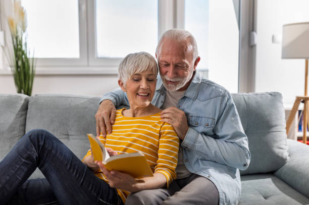 istock Senior couple in love reading book on sofa at home 1491944100
