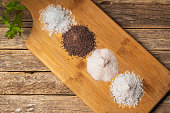 Wooden table with piles of different types of salt, black, pink, flake and seasoned with truffle, on a rustic wooden background. Top view.