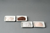 Small bowls with different types of salt, black, pink, flake and seasoned with truffle, on a gray background.