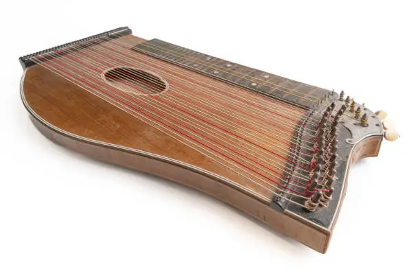 High angle closeup horizontal studio shot of vintage, old wooden zither isolated on white background. Detail of zither mechanics and tuning pins. Dusty and scratched instrument