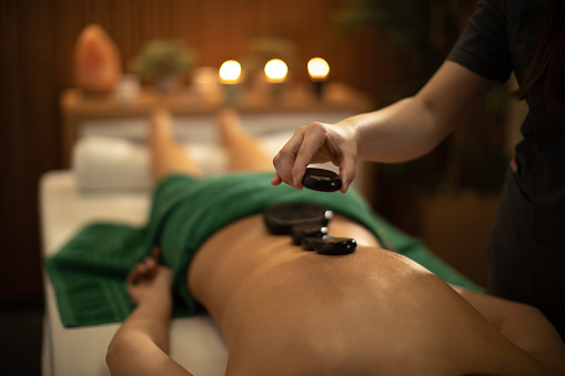 Beautiful young woman receiving relaxation back massage with hot lava stones in spa salon. She has a nice healthy skin and looks beautiful and very attractive.