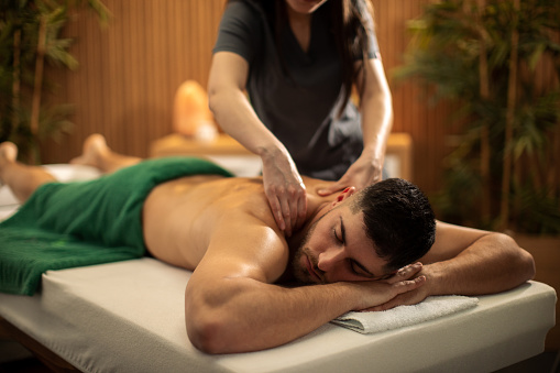 Happy man receiving back and shoulder relaxational massage by professional therapist in beautiful spa center