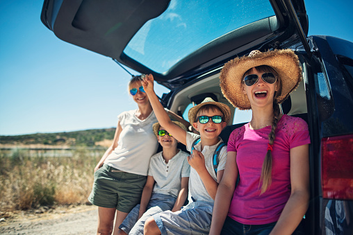 Mother and kids enjoying travelling by car. Family is having a break and the car is parked on the side on the road. \nThe car details has been removed or modified.\nNikon D810