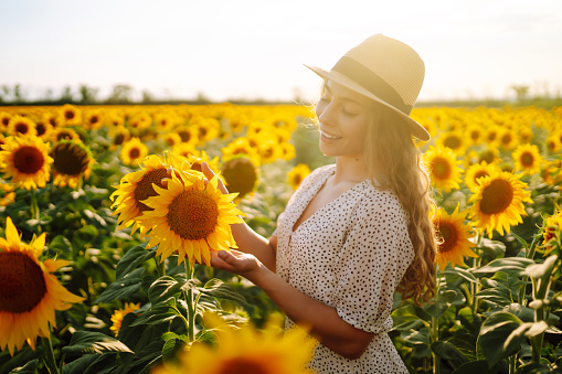 Happy young woman surrounded by yellow sunflowers in full bloom, in a flower garden,