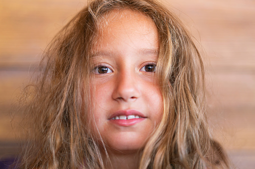 Portrait of attractive caucasian little child girl with blond curly hair and cute smile. Happy smiling child looking at camera - close-up, outdoors.