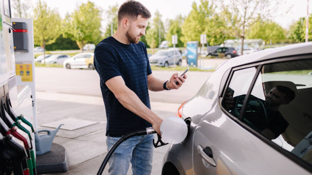 Bearded man refuelling car on gas station and looking into his smartphone. Man compares fuel prices stock photo