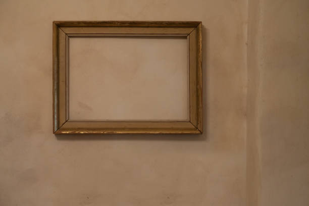 istock Empty frame with no painting in it hanging on a pale orange wall with Venetian stucco. Art home interior concept with copy space. 1491985609