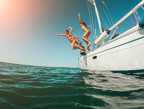 Happy friends diving from sailing boat into the sea - Soft focus on left girl face