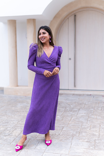 Vertical photo of a model posing with elegant purple dress outside a building