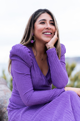 Vertical portrait of a happy woman in purple cocktail dress siting outdoors