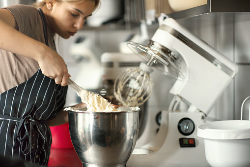 Closeup of unrecognizable women mixing a cake batter inside of a big plastic bowl.