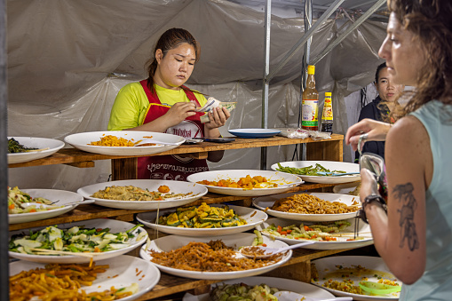 Night Market, Luang Prabang, Laos - March 12th 2023: Woman counting her money in a street kitchen at the famous night market in the center of the city