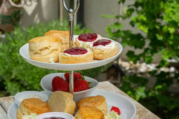 food, pastry, baked scones with raspberry jam, clotted cream and strawberries on an etagere in garden, afternoon tea