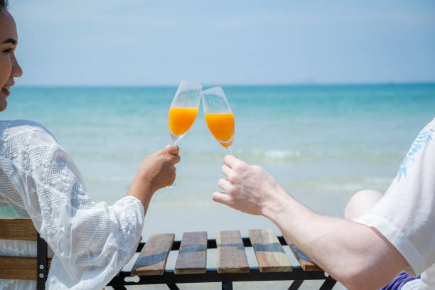 istock Smiling couple enjoying drinks orange juice while resting on comfortable chairs by sea beach,Summer vacation or honeymoon concept. 1491996272