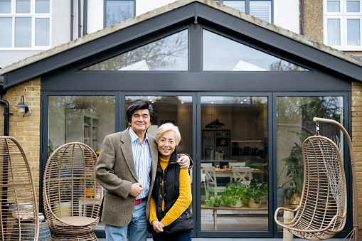 Contented Asian husband and wife together in back garden by modern patio doors