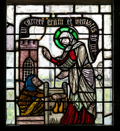 Ancient medieval stained glass window in a gothic Christian church. Hospital mercy scenes with saints