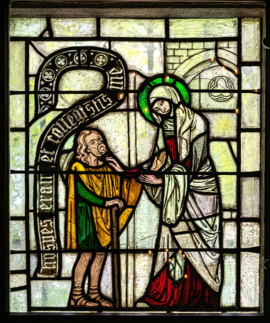 Ancient medieval stained glass window in a gothic Christian church. Hospital mercy scenes with saints