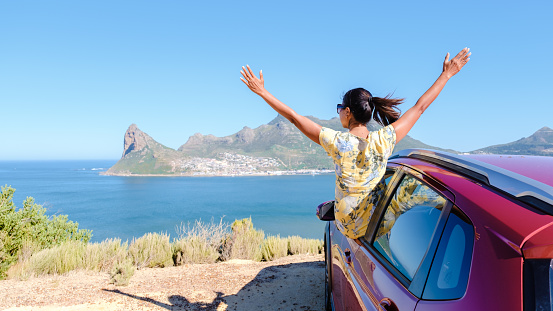 woman outside a car window with hands up, a car at Chapmans Peak Drive in Cape Town South Africa looking out over the ocean. women on a road trip garden route South Africa with renal car