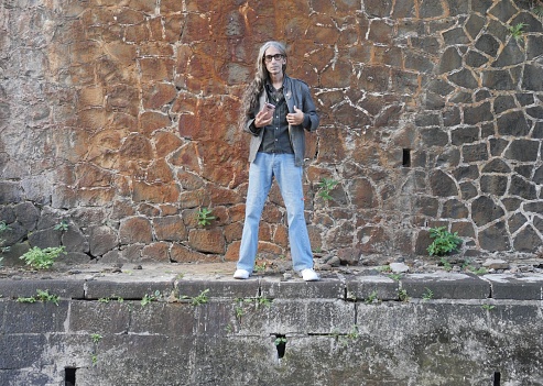 Long haired man posing in front of antique stone drains and orange wall