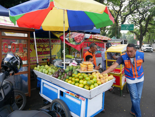 A man selling freshly and cut tropical fruit from a traditional Indonesian food cart or grobak on the roadside in Bandung, West Java, Indonesia. The fruits include mango, haru manis mango, jeruk oranges, avocados and apples etc. May 21, 2023 - Bandung, West Java, Indonesia.
A man selling freshly and cut tropical fruit from a traditional Indonesian food cart or grobak on the roadside in Bandung, West Java, Indonesia. The fruits include mango, haru manis mango, jeruk oranges, avocados and apples etc. fruit cart vendor stock pictures, royalty-free photos & images