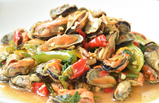 spicy stir fried mussel with slice onion and basil leaf on plate
