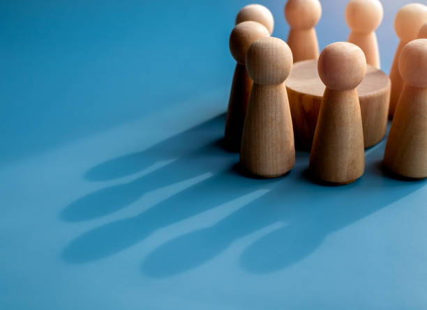 istock Close-up small standing wooden human figures made a crown shape shadow on blue background. Business goal and success, leadership, teamwork power and confidence concepts. 1492022191