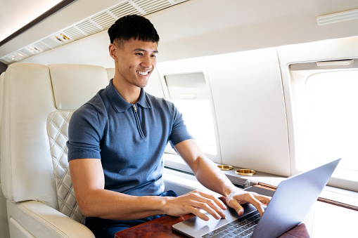 Early 30s executive in casual attire smiling while using laptop during flight.