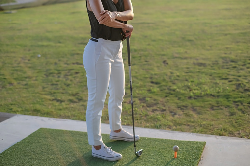 Close-up shot of unrecognizable mature Asian woman suffering golfer elbow in a driving range