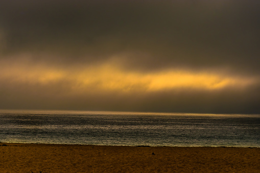 view of the sand, the sea and the sky, on a completely cloudy afternoon in which the sun filters at sunset on the coast of Papudo, Valparaíso Region, Chile