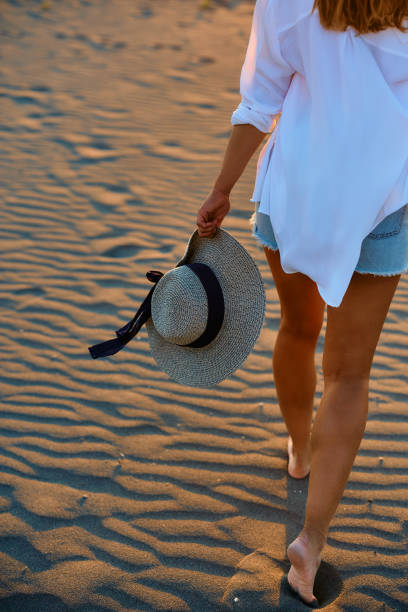 Rear view of woman walking on the sand while enjoying in summer sunset at the beach.